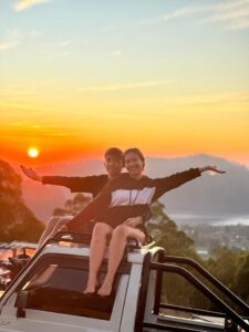 Two people taking photos on a jeep as the sun begins to rise.